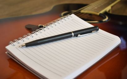 A notepad and pen resting on a guitar